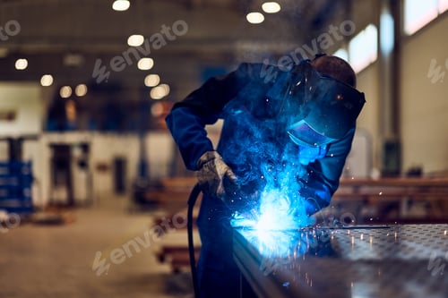 Preview: Worker Welding Metal in Industrial Workshop with Bright Sparks and Blue Light
