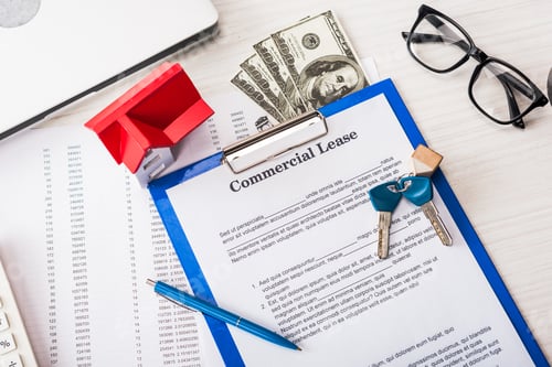 Preview: top view of document with commercial lease lettering on clipboard near keys, money, house model, pen