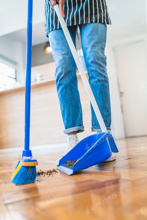 Preview: Latin man sweeping wooden floor with broom at home.