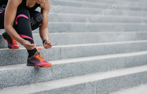 Preview: Urban activity. African american woman in sportswear tying laces on sneakers for workout