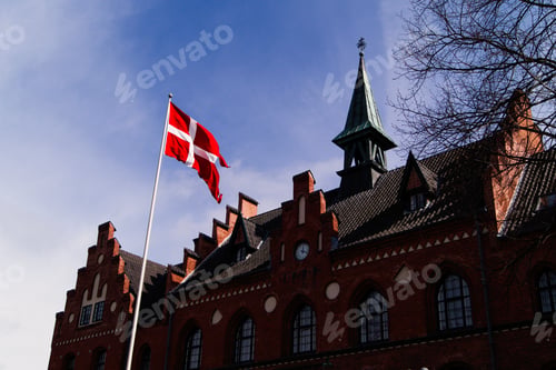 Preview: Historic Danish building with national flag waving against a bright blue sky, Hillerød, Denmark.