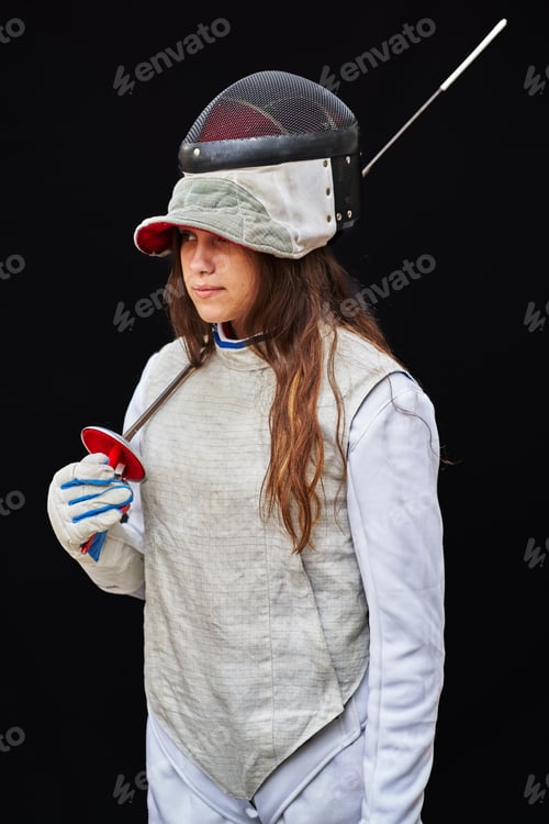 Preview: Portrait of woman dressed in white fencing costume practicing with the sword on black background.