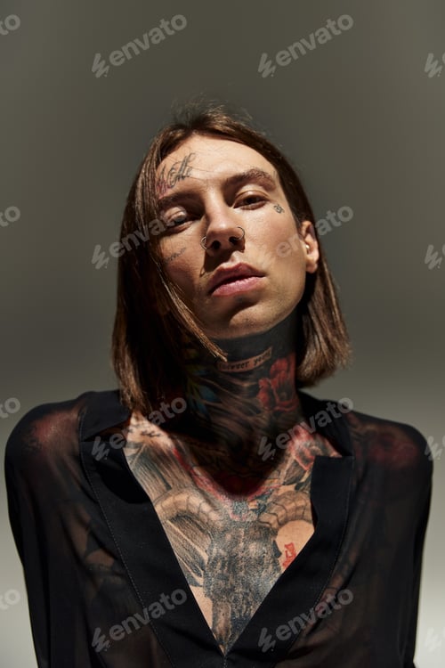 Preview: good looking young man in black blouse with tattoos and piercing looking at camera, fashion