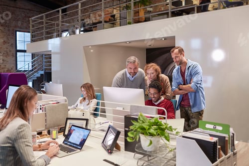 Preview: Colleagues looking over shoulder of young man working in modern office