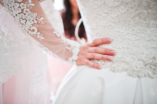 Preview: Close-up photo of bride's hand on her waist, holding wedding dress.