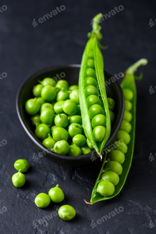 Preview: Green peas in black ceramic bowl with scattered pods