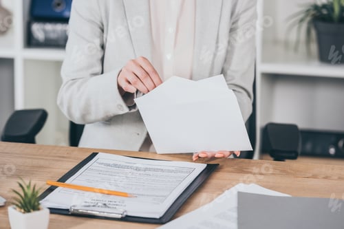 Preview: cropped view of businesswoman putting money into open envelope while sitting at desk, compensation
