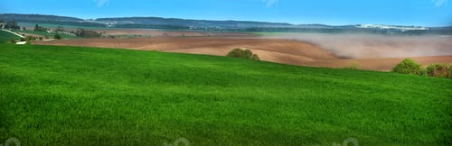 Preview: panoramic view of green fields winter wheat and clouds of dust on the hills of plowed lands,