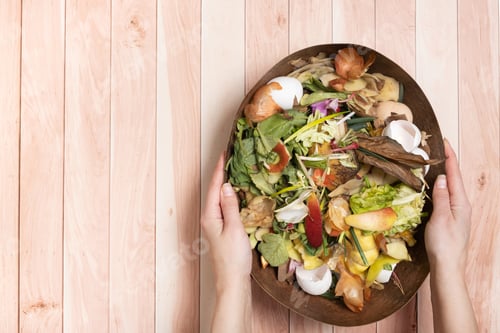 Preview: Organic garbage for compost in female hands on wooden background. Composting concept