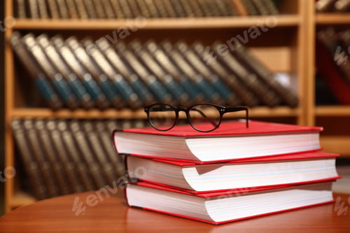 Preview: Stack of books and glasses on table in library. Space for text