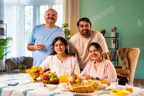 Preview: Having breakfast while smiling together, Indian family looks at camera with joy at home