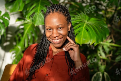 Preview: Cheerful optimistic African American woman smiling at camera surrounded by green tropical plants.