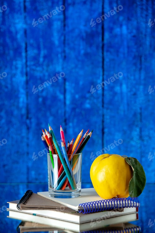 Preview: Vertical view of colored pencils kept in a glass jar and quince with stem on stacked spiral