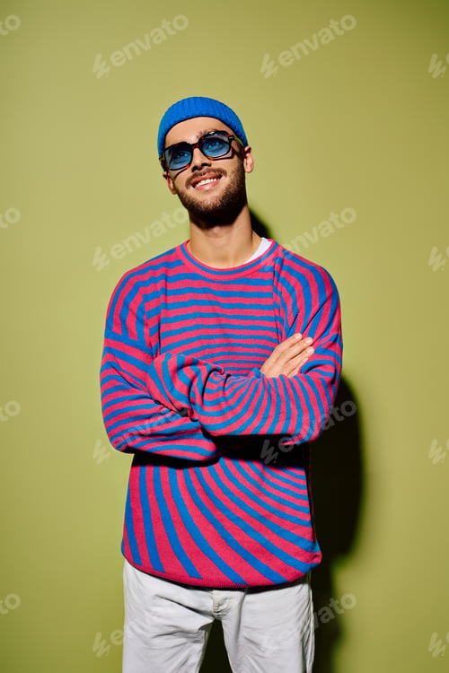 Preview: Fashionable young man in vibrant attire stands confidently against a green backdrop