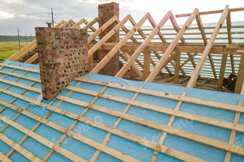 Preview: Aerial view of a brick house with wooden roof frame under construction