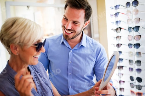 Preview: Health care, people, eyesight and vision concept. Mature woman choosing glasses at optics store