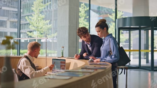 Preview: Smiling couple talking hotel reception. Joyful clients checking in writing forms