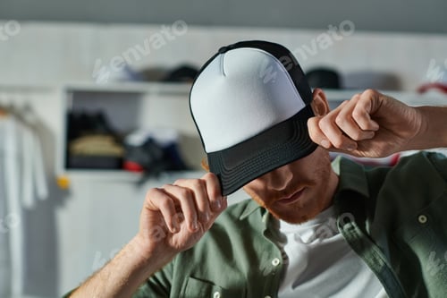 Preview: Young craftsman covering face and wearing snapback while standing and working in blurred print