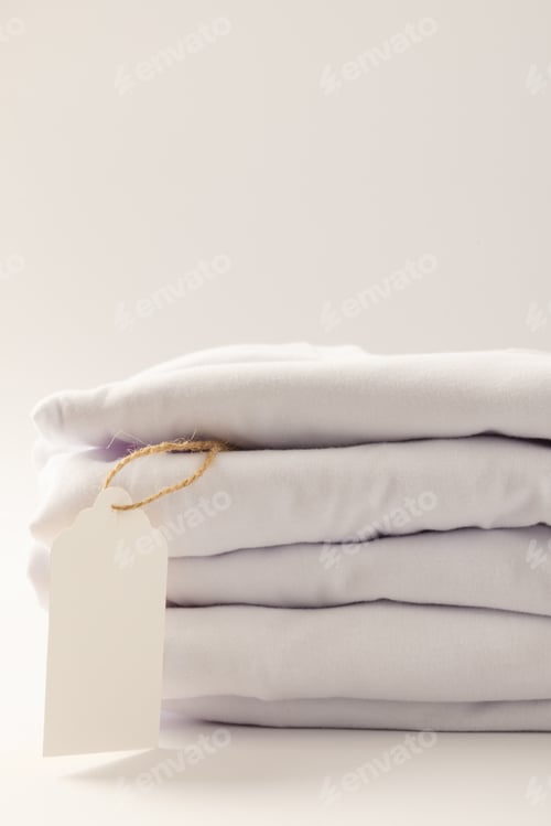 Preview: Stack of white t shirts with tag and copy space on white background