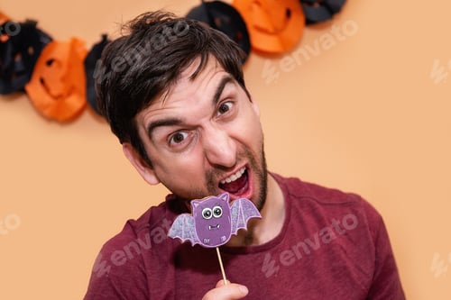 Preview: Guy trying to eat gingerbread in the form of purple bat. Halloween treat. Young man is having fun