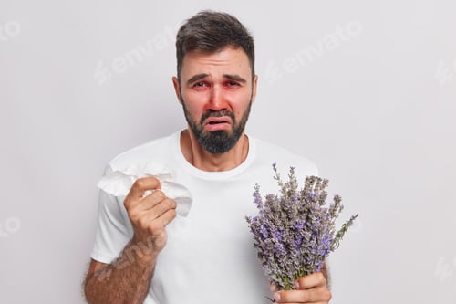 Preview: Puzzled unhappy bearded adult man has runny nose holds handkerchief cannot stop sneezing has allergy