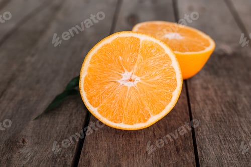 Preview: Halves of orange fruit on gray wooden background. Orange pulp and green leaves