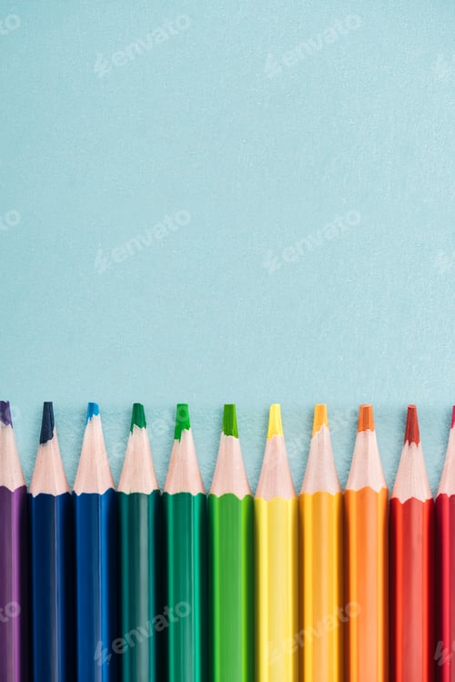 Preview: top view of rainbow multicolored pencils arranged in horizontal line on blue background, lgbt