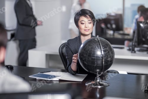 Preview: Woman looking at globe sitting at desk in city office