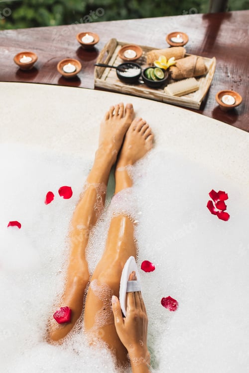 Preview: Woman washing legs in bath tub with foam bubbles and use natural loofah sponge. Spa treatment, body