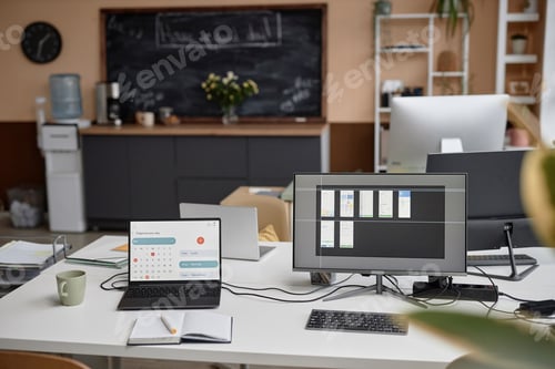 Preview: Laptop and Computer at Workplace Table in Office with Blackboard