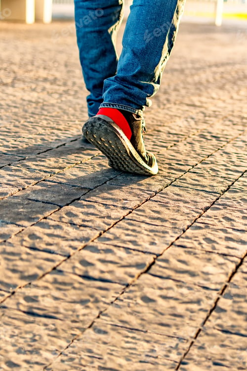 Preview: Close up of man sneakers on street, with sunset and sunlight background.