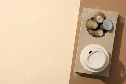 Preview: Coffee capsules and paper cup in paper stand on brown and beige background, space for text