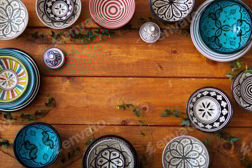 Preview: Assorted colorful ceramic bowls on a wooden background adorned with green leaves.