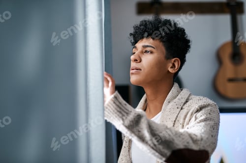 Preview: Shot of a young man opening his bedroom curtains in the morning at home