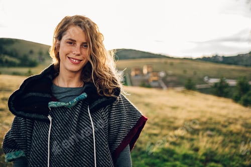 Preview: Portrait of a stylish woman hiking on a mountain path with tall grass.