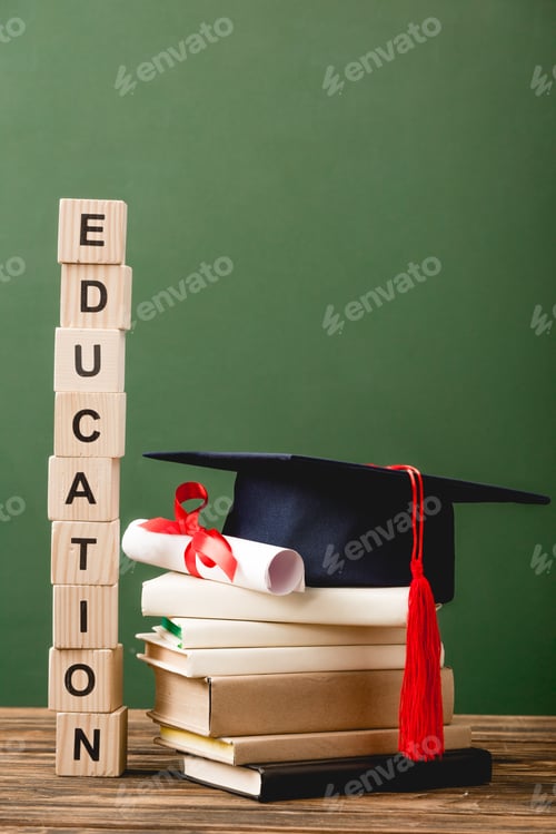 Preview: wooden blocks with letters, books, academic cap and diploma on wooden surface isolated on green