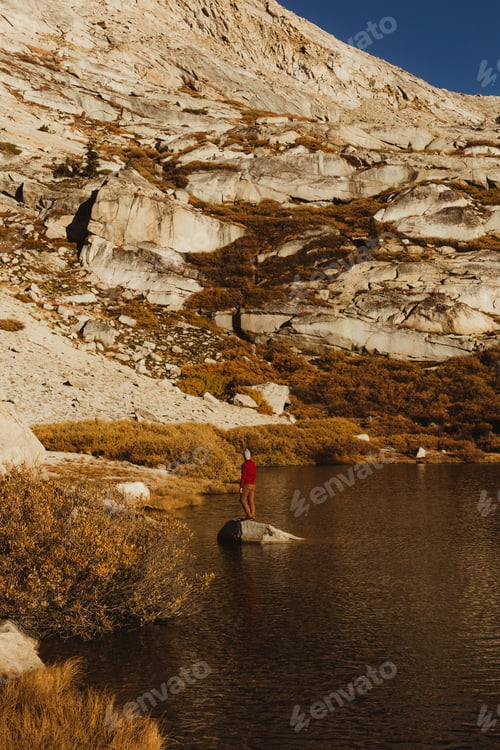 Preview: Hiker standing on a rock by a mountain lake at sunset.