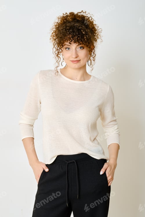Preview: Curly-haired woman poses in a cozy outfit against a light background in a studio setting