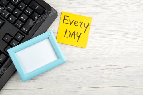 Preview: Overhead view of blue empty picture frame and every day note half shot laptop on white stripped