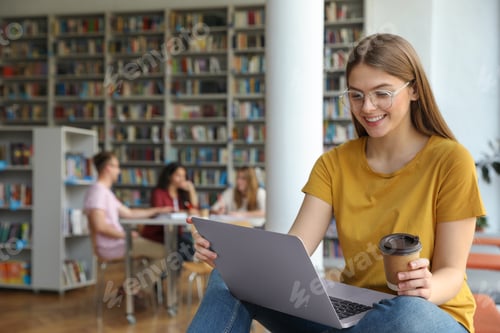 Preview: Young woman working on laptop in library. Space for text