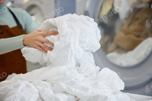 Preview: Female worker is loading clothes into a washing machine at a laundromat