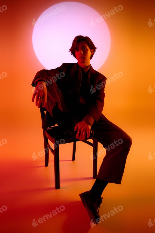 Preview: Stylish young man poses on a chair against a vibrant, colorful background