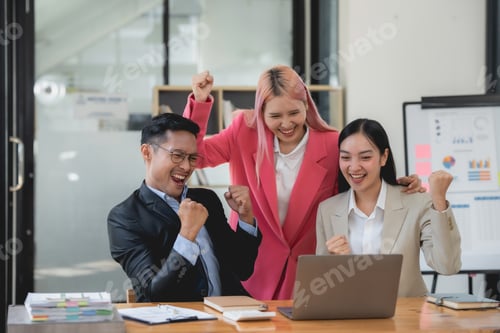 Preview: Triumphant asian business team with raised fists celebrating success at the office.