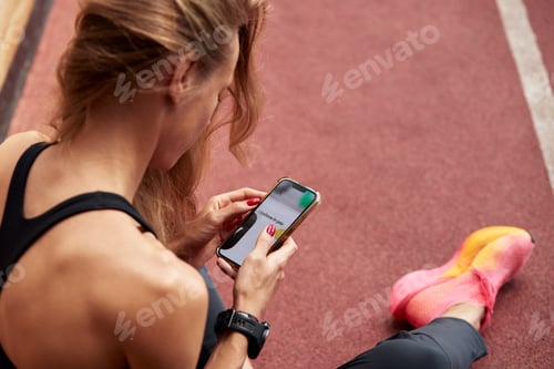 Preview: Young athlete girl is having break after a workout in the stadium. A slender attractive blonde in a
