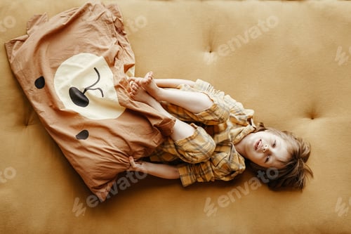 Preview: Bed vibes. Top view of a happy boy lying on yellow mattress and hugging his favorite pillow
