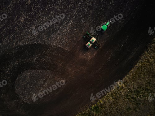 Preview: Aerial view of a two modern green tractors plowing dry agricultural field
