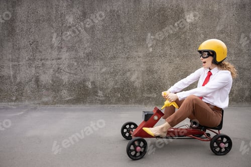 Preview: Funny businesswoman driving retro pedal car outdoor