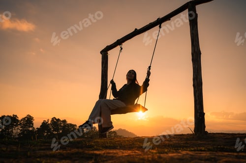 Preview: Silhouette traveler asian woman sitting with playing wooden swing on mountain at the sunset