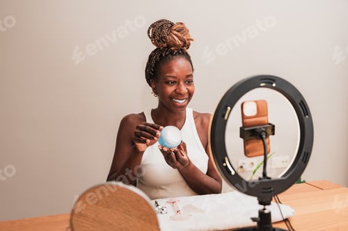 Preview: female influencer recording vlog video live streaming at home holding demonstrating cosmetic