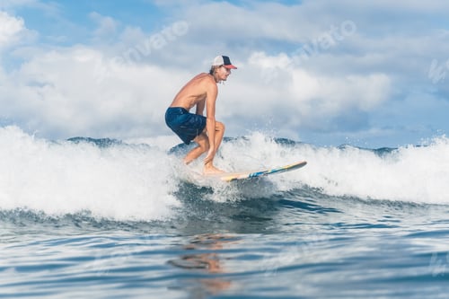 Preview: man in swimming shorts and cap surfing in ocean